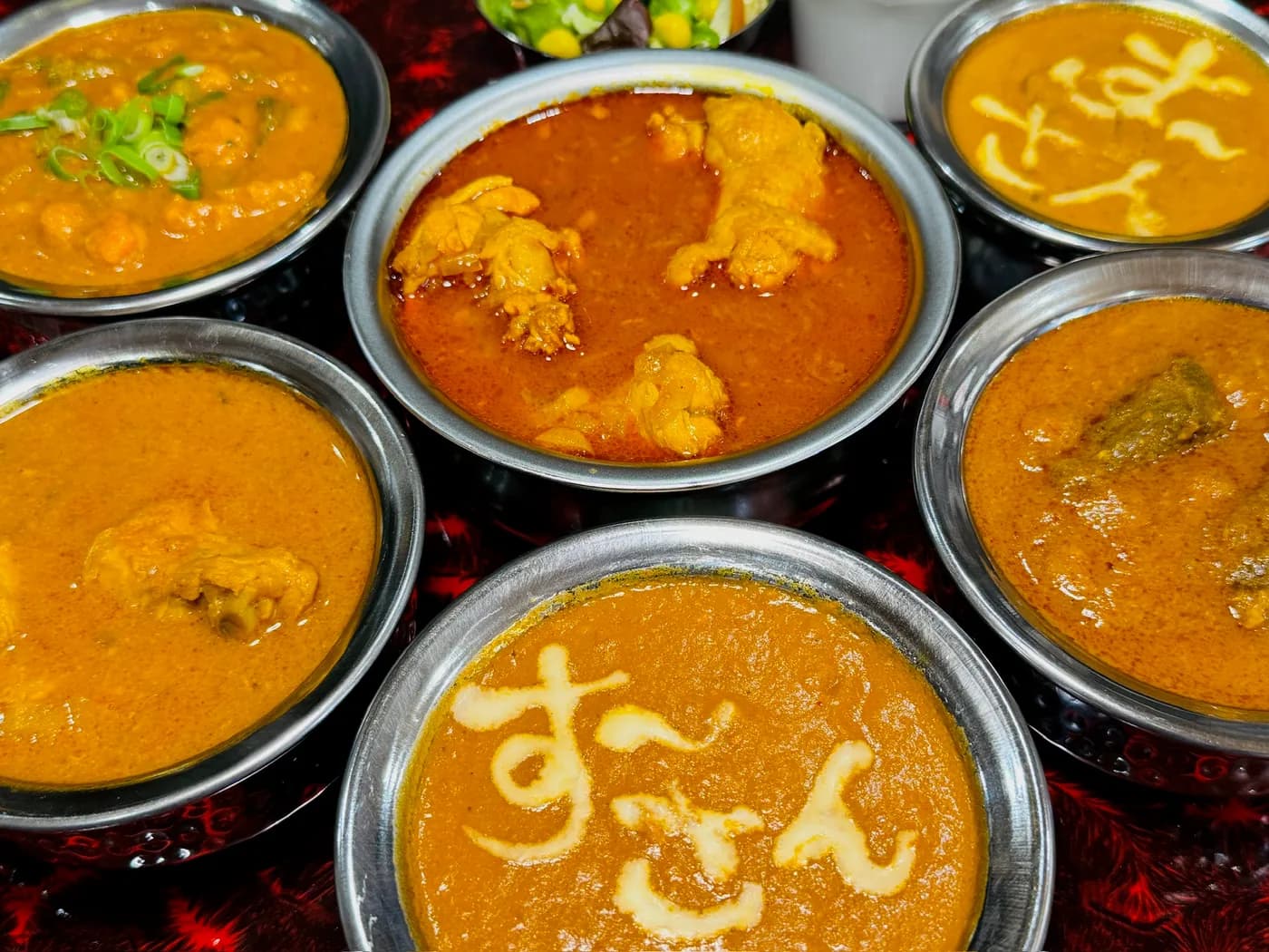 Six Namaste Surya curries in steel bowls, two finished with the restaurant's name piped in cream