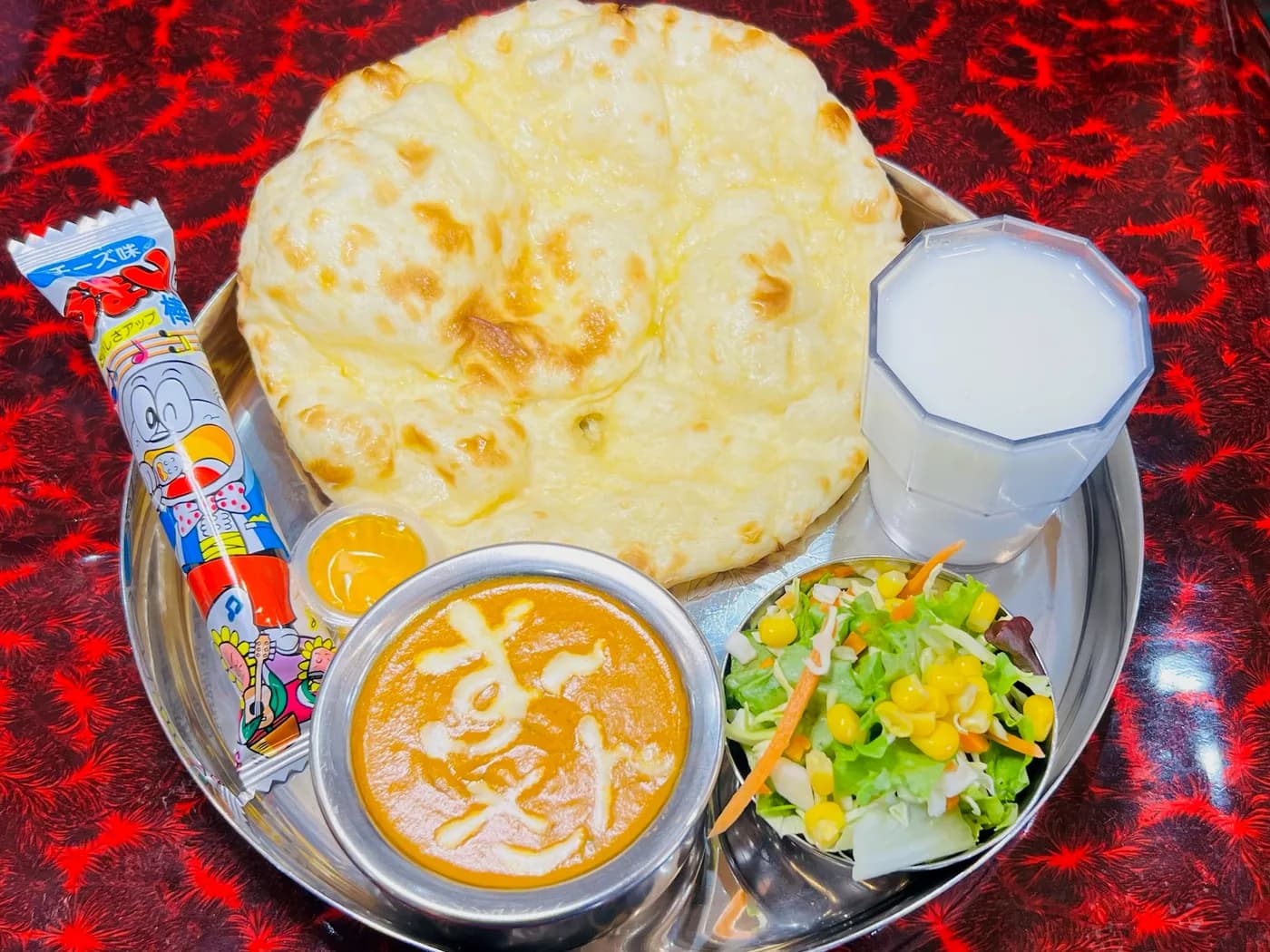 A children's set on a steel tray: cheese naan, mild curry, salad, lassi and a sweet