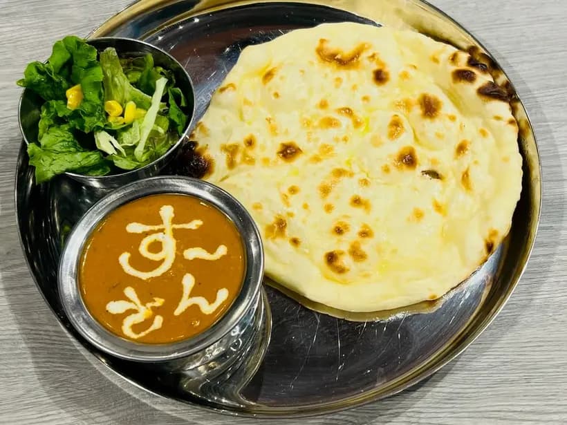 A vegetarian set: cheese naan, curry finished with the restaurant's name in cream, and salad