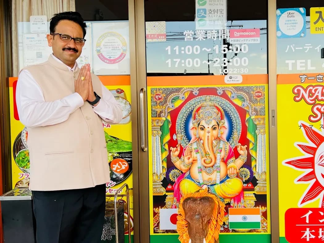 Su-san greeting guests with hands together at the entrance to Namaste Surya